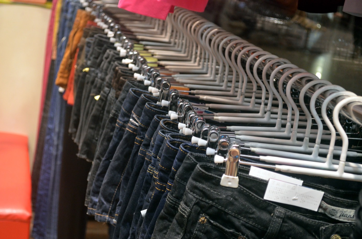 A rack of dark denim jeans hanging in a row from white hangers