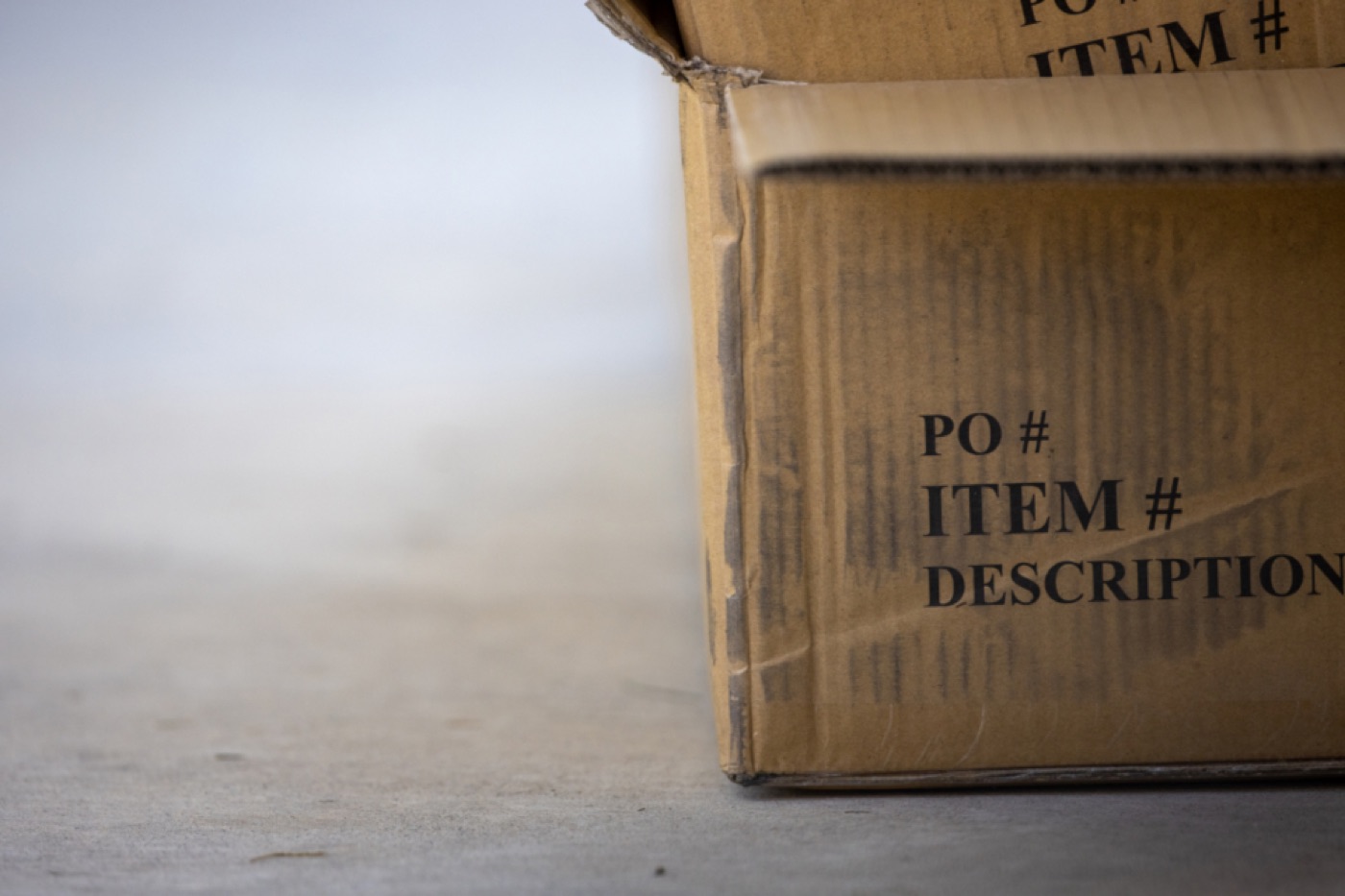 A worn cardboard box sitting open on a concrete floor, its top flaps folded back