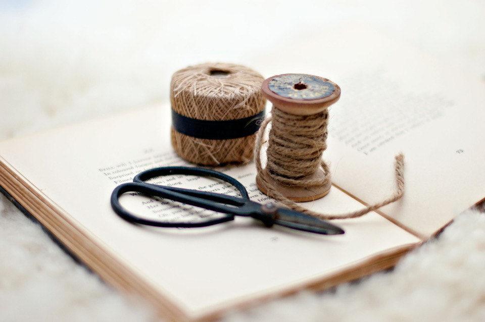 Two spools of natural jute twine and a pair of black craft scissors resting on an open book
