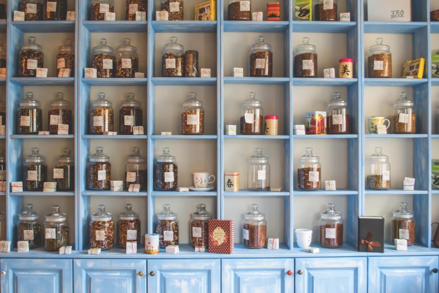 Blue wooden shop shelves lined with glass jars of loose goods, each with a hand-tied paper label, and small wrapped gift boxes along the ledges