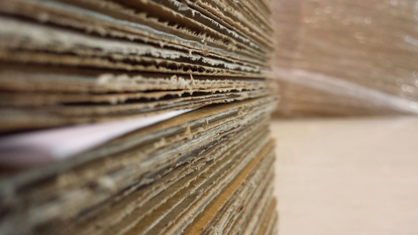 A stack of flat, unfolded cardboard boxes seen edge-on, waiting to be built