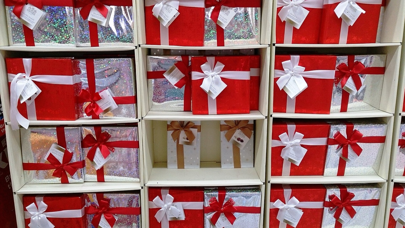 Rows of gift boxes wrapped in red and holographic silver paper, each tied with a red or white ribbon bow, on white shelves