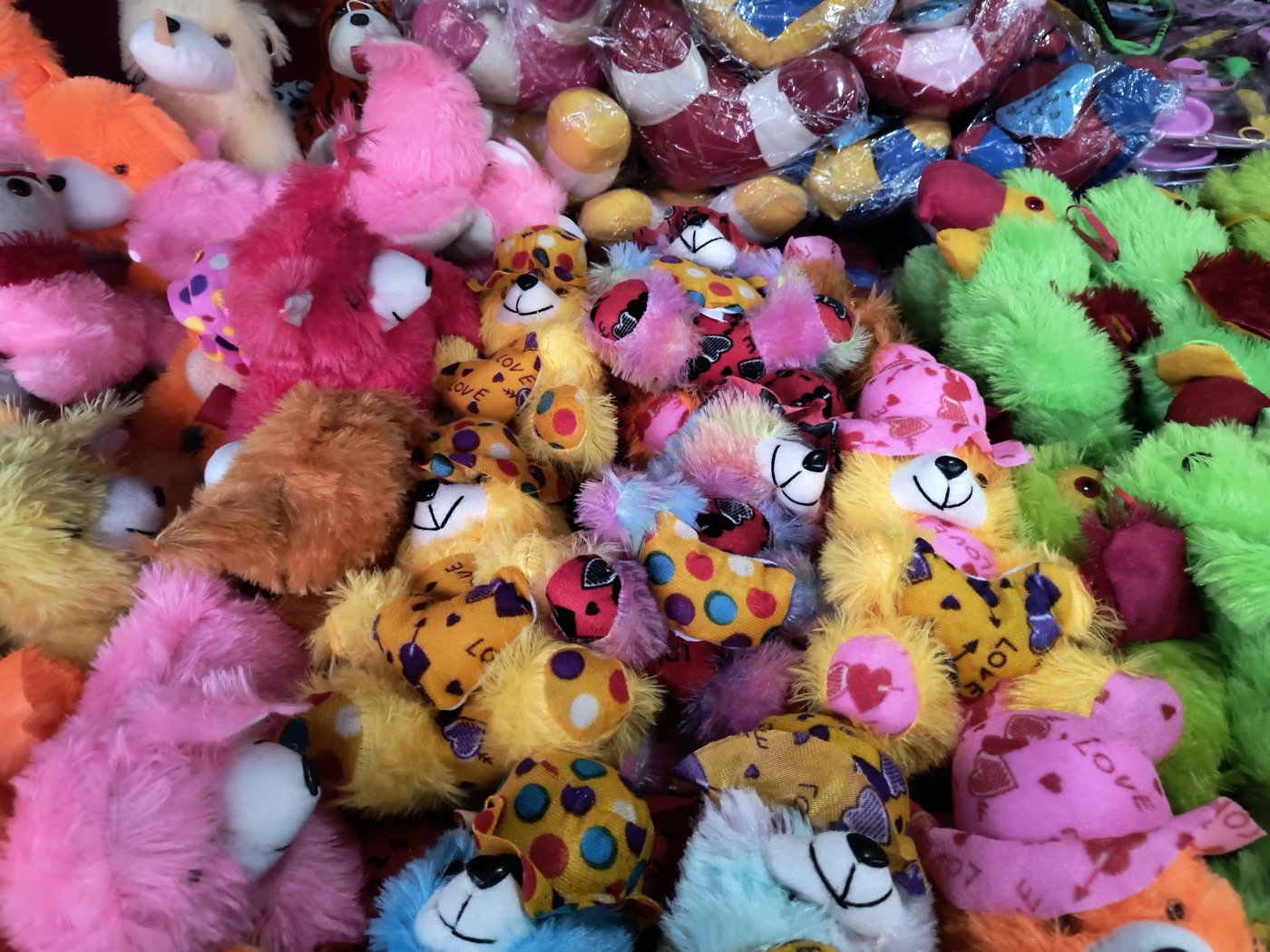 A tightly packed pile of colorful plush bears and animals in pink, yellow, green and orange, some wearing hats