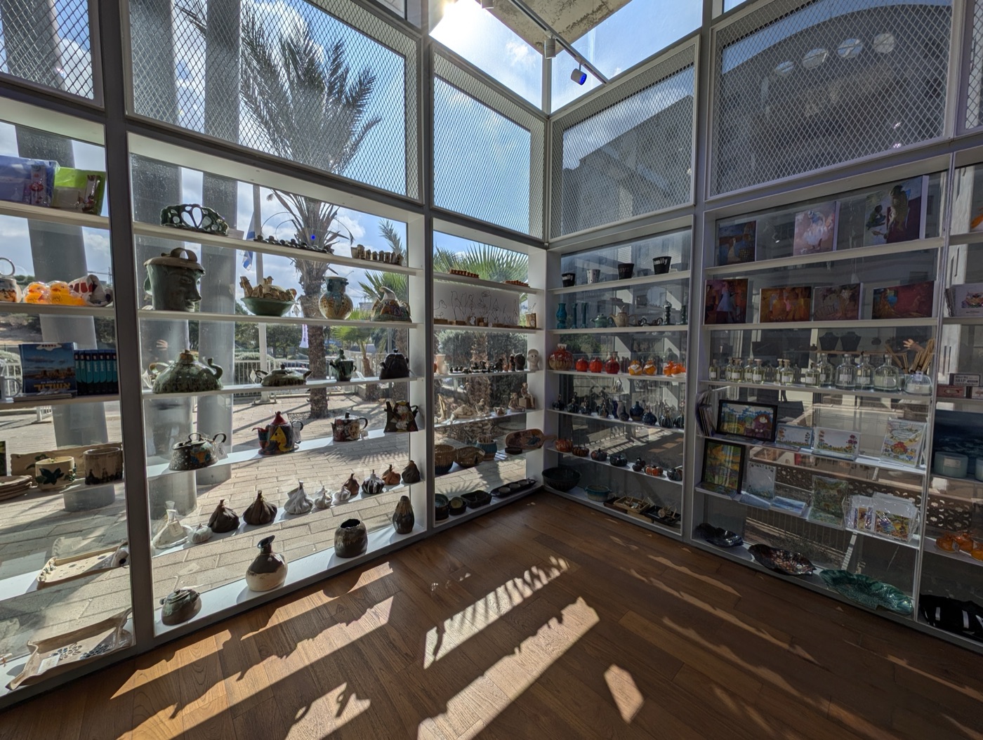 Sunlit white display shelves in a small shop, holding ceramic teapots, bowls, glass bottles and framed prints