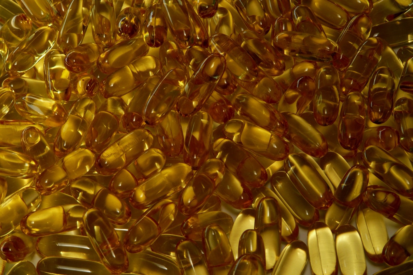 Close-up of a pile of amber softgel capsules with light shining through them