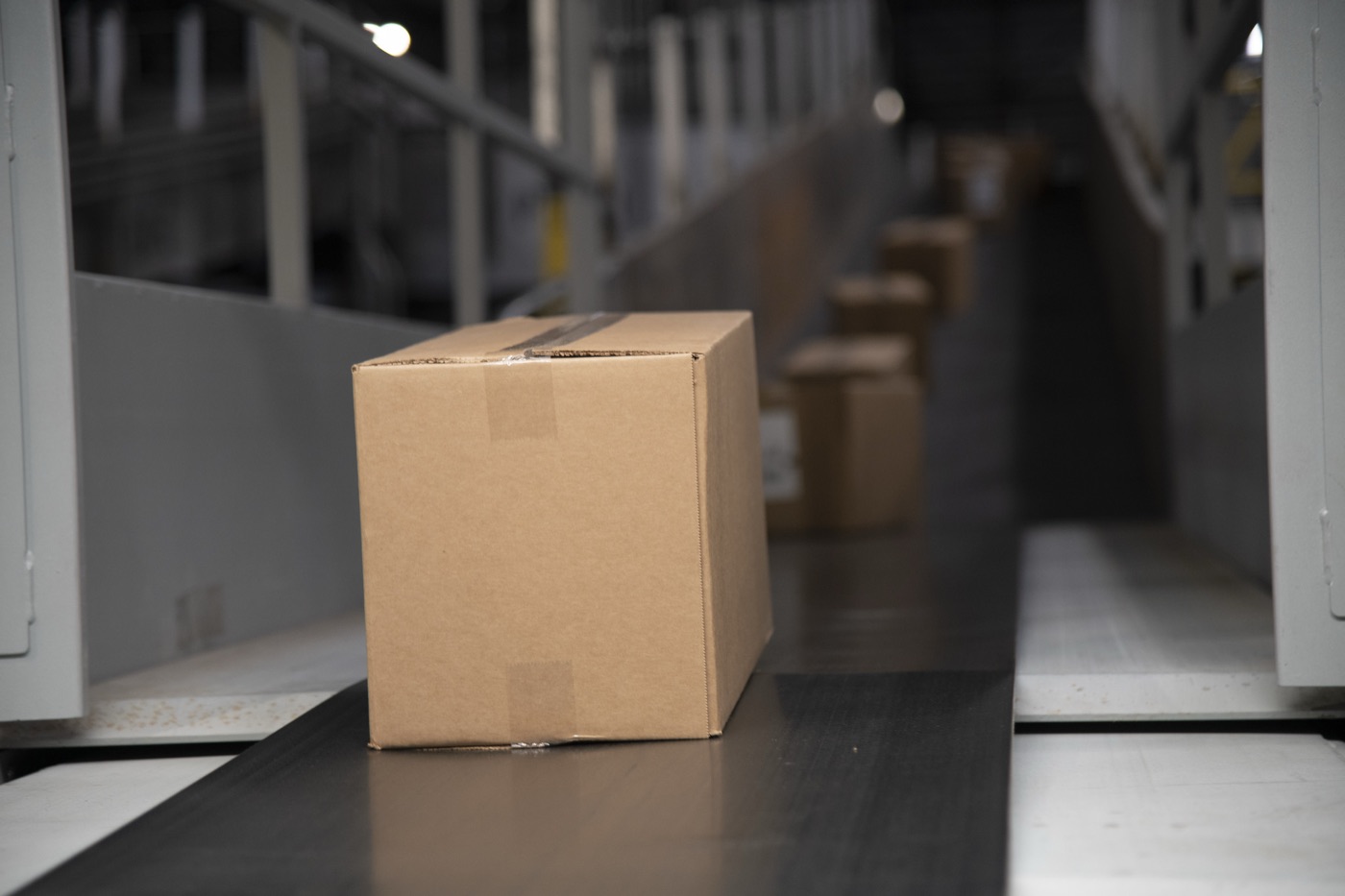A taped cardboard box on a conveyor belt, with more boxes lined up behind it
